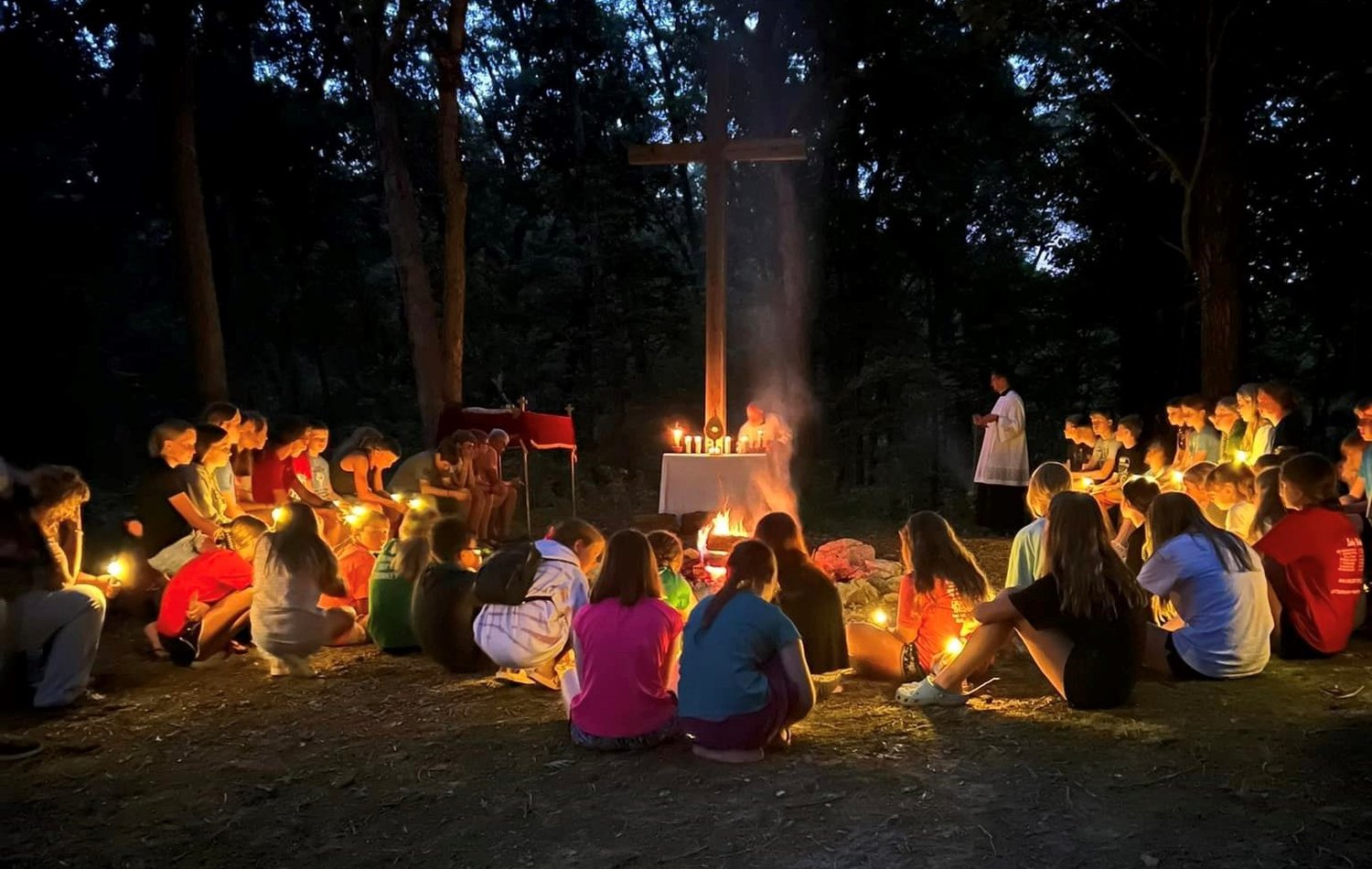 Participants in the Camp Tolton Catholic camp for young people gather for Adoration of the Most Blessed Sacrament by firelight following a Eucharistic procession to a wooded area at Camp Jo’Ota in Clarence.